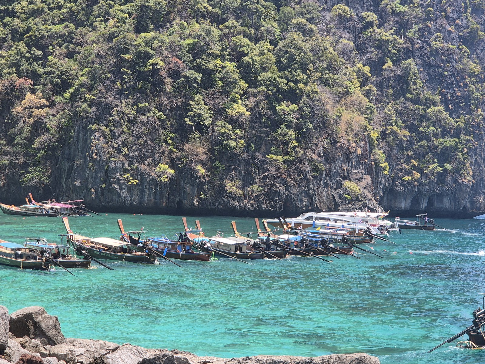 Boats on turquoise water below a green rocky cliff