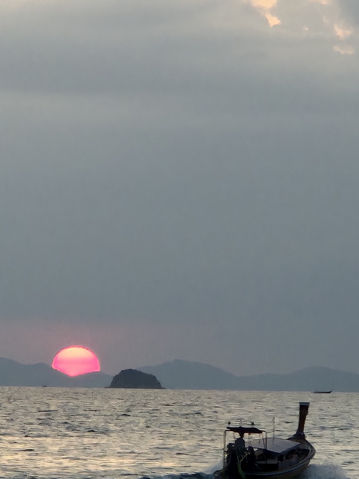Red sun setting over the sea beside a silhouetted boat
