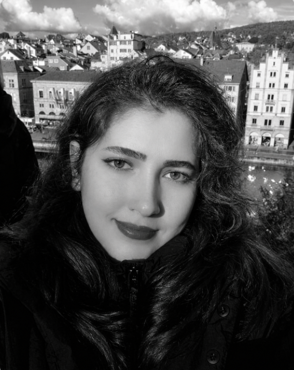 Black-and-white portrait of Romina Veisy, with a hillside town behind her